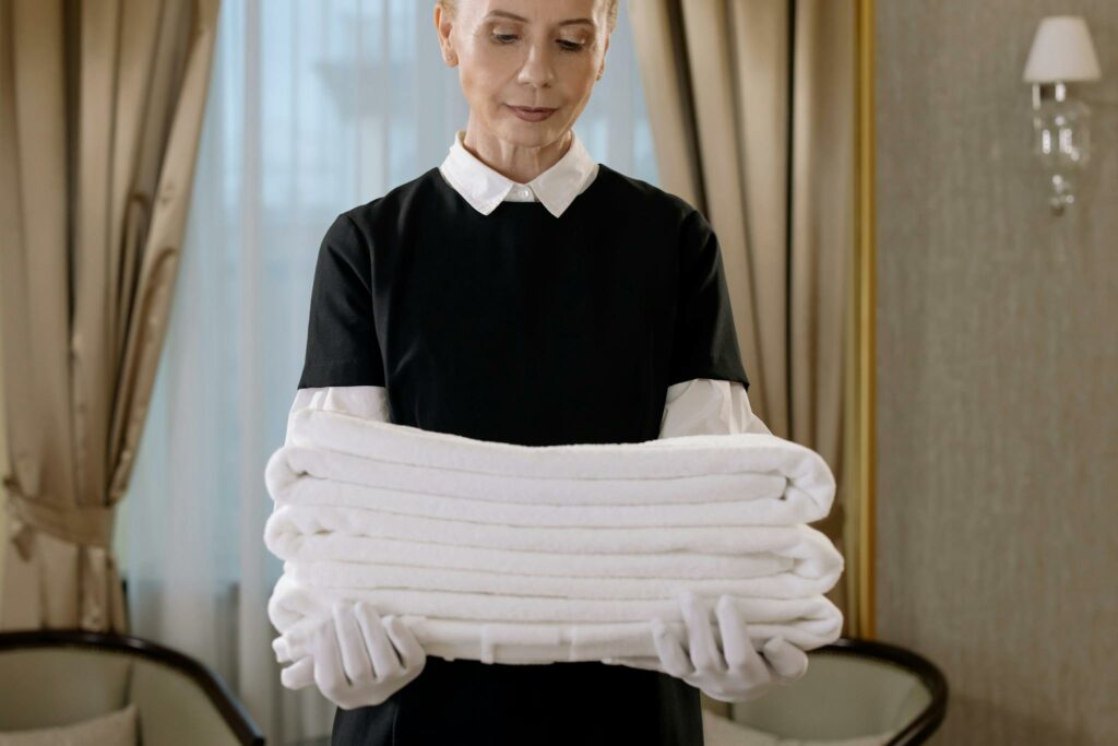Woman in Black and White Uniform Holding a Stack of Towels